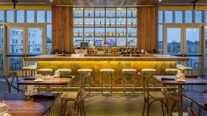 A bar area with a marble counter, wooden chairs, and a large window with bottles.