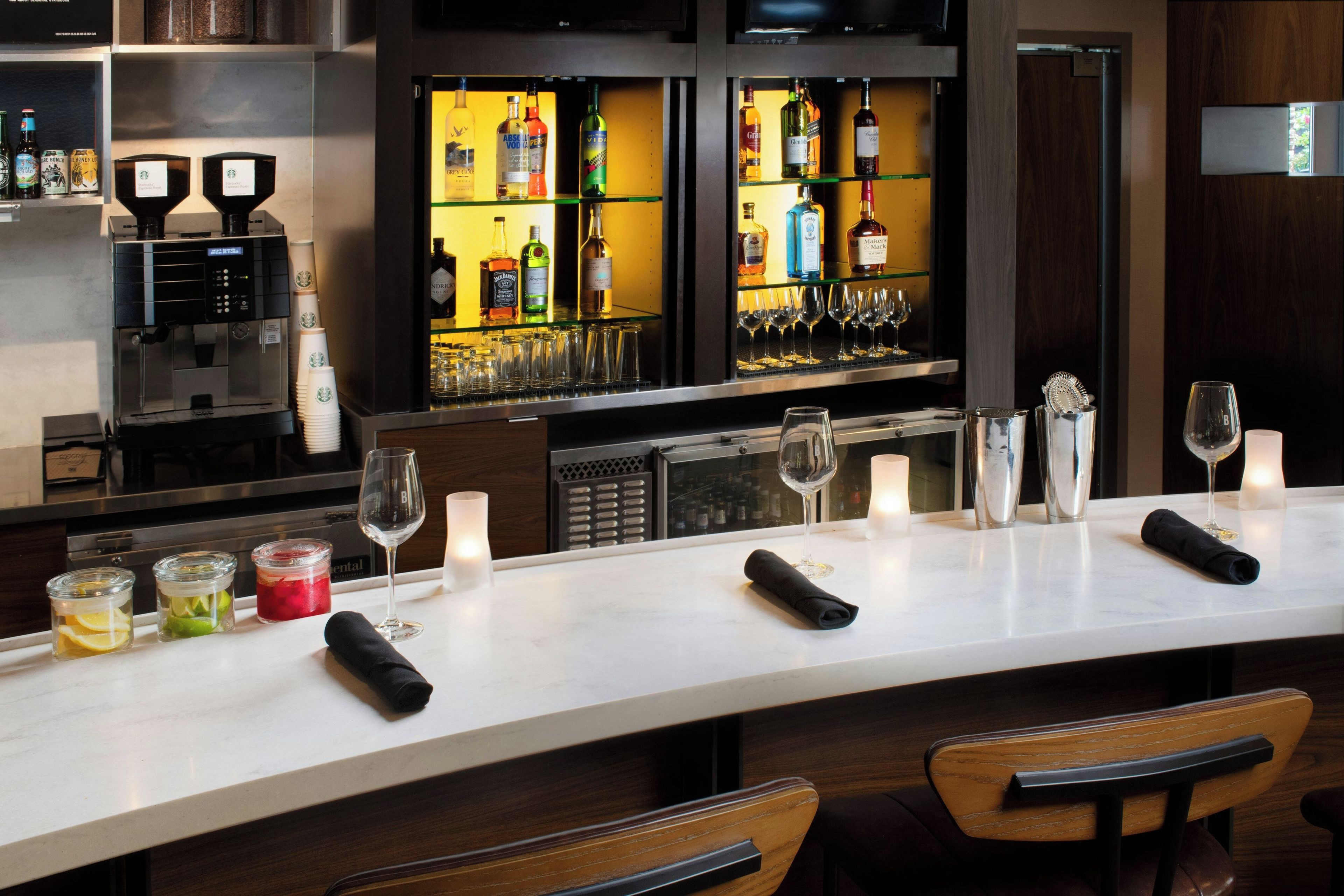 Een bar met een lange toonbank, diverse glazen, flessen en een koffieapparaat.
