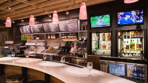 Un espace bar avec un long comptoir, des tabourets, un écran de télévision et un tableau affichant le menu.