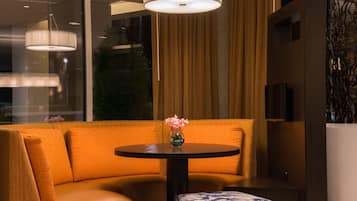 Un interior moderno con un sofá, una mesa redonda con un jarrón de flores y un ventanal con cortinas.