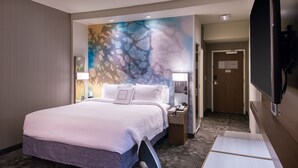 Une chambre d’hôtel avec un grand lit, un bureau, une chaise, une table de chevet, une lampe et un téléviseur.