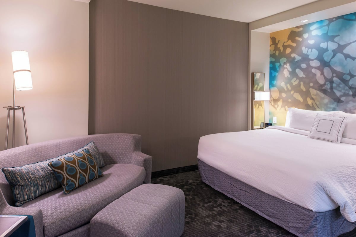 A hotel room with a bed, a sofa, and a lamp.