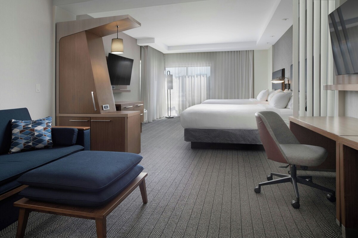 A hotel room with a bed, a desk, a chair, a TV, and a sofa.