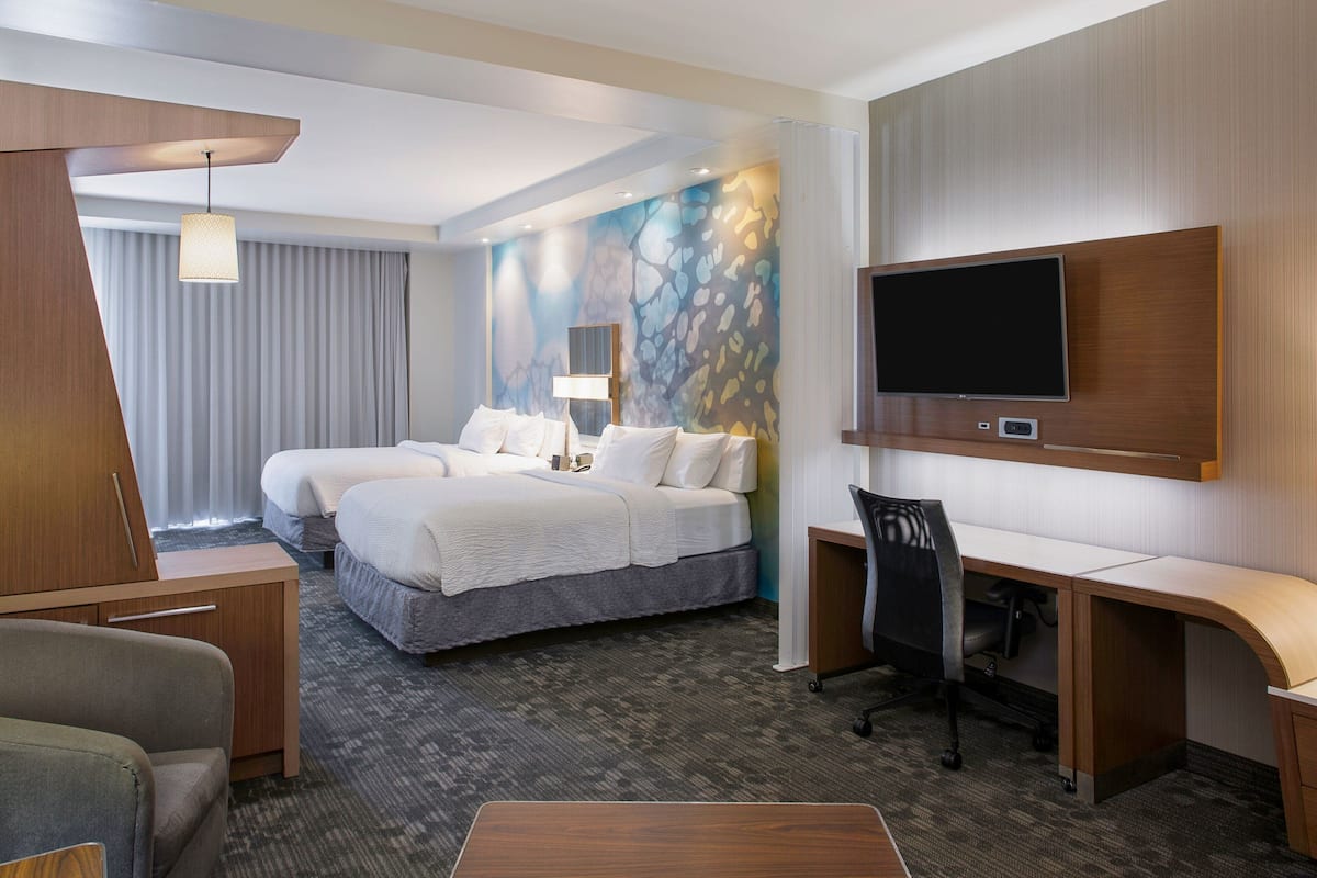 A hotel room with a large bed, two bedside tables, a desk, a chair, a flat-screen TV, and a wall-mounted TV.