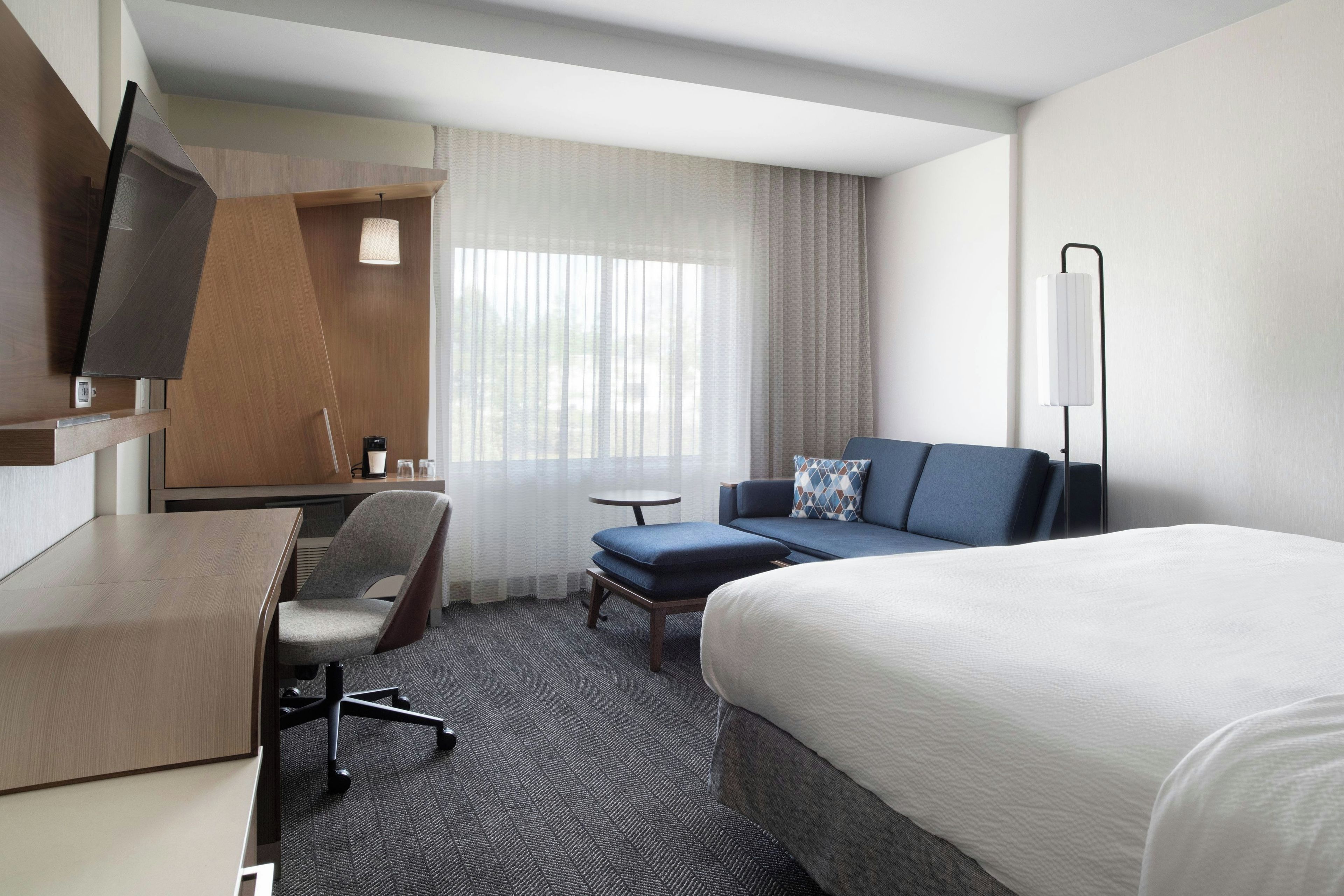 A hotel room with a bed, a desk, a chair, a sofa, and a television.