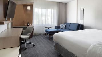 A hotel room with a bed, a desk, a chair, a sofa, and a television.