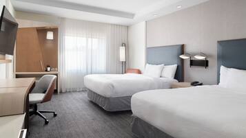 A hotel room with two beds, a desk, a chair, and a television.