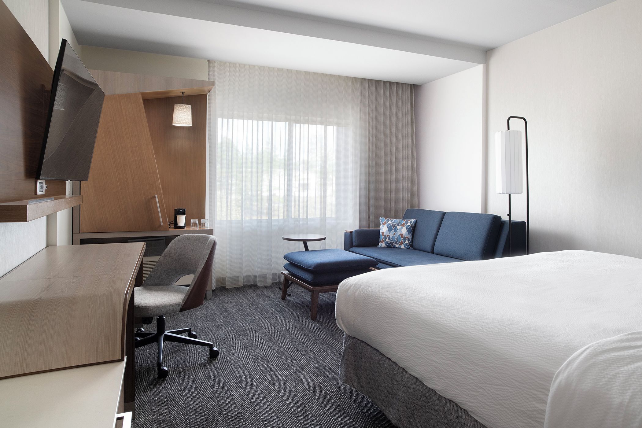Habitación de hotel con cama, escritorio, silla, mesita y televisor.