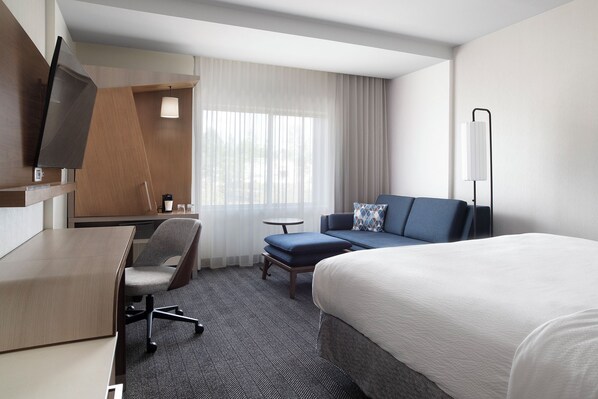 Habitación de hotel con cama, escritorio, silla, mesita y televisor.