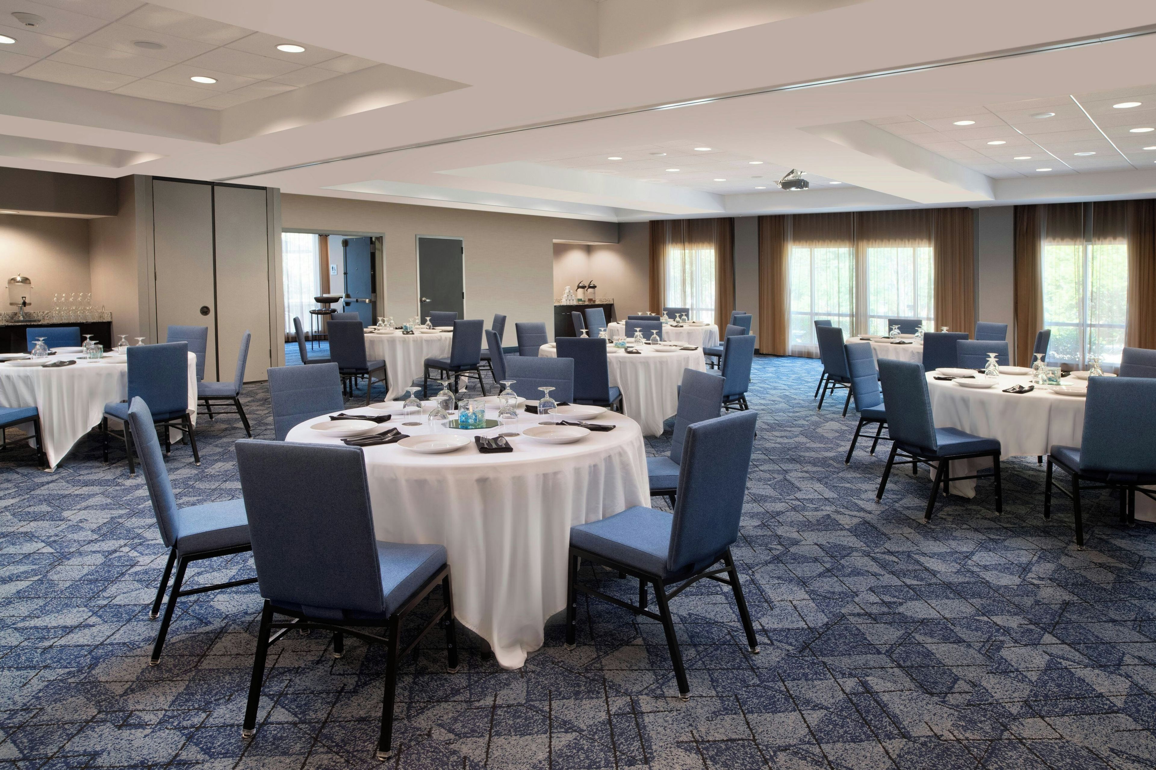 A conference room with round tables, chairs, and a carpeted floor.