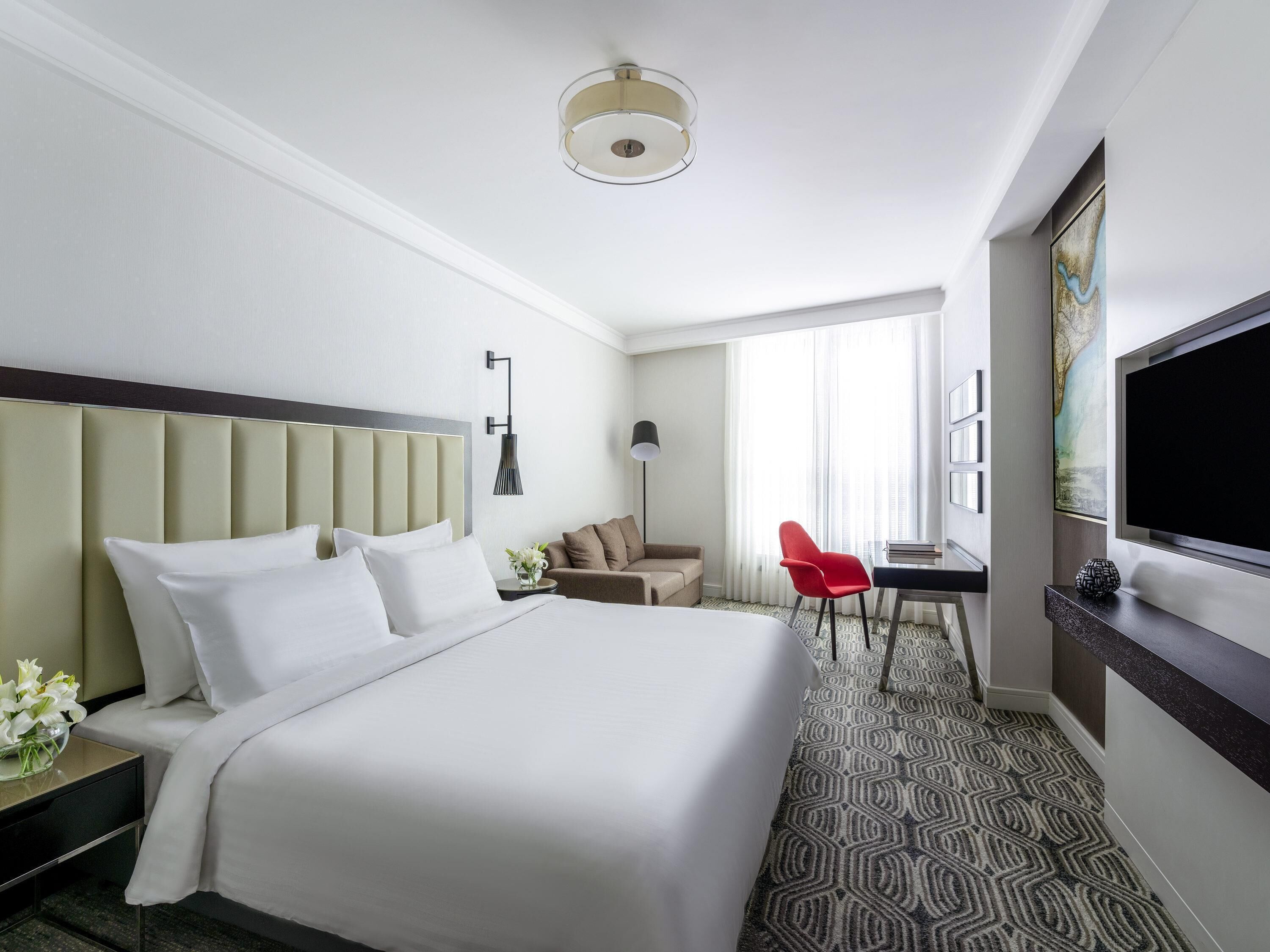 A hotel room with a large bed, a desk with a chair, a TV, and a window with curtains.