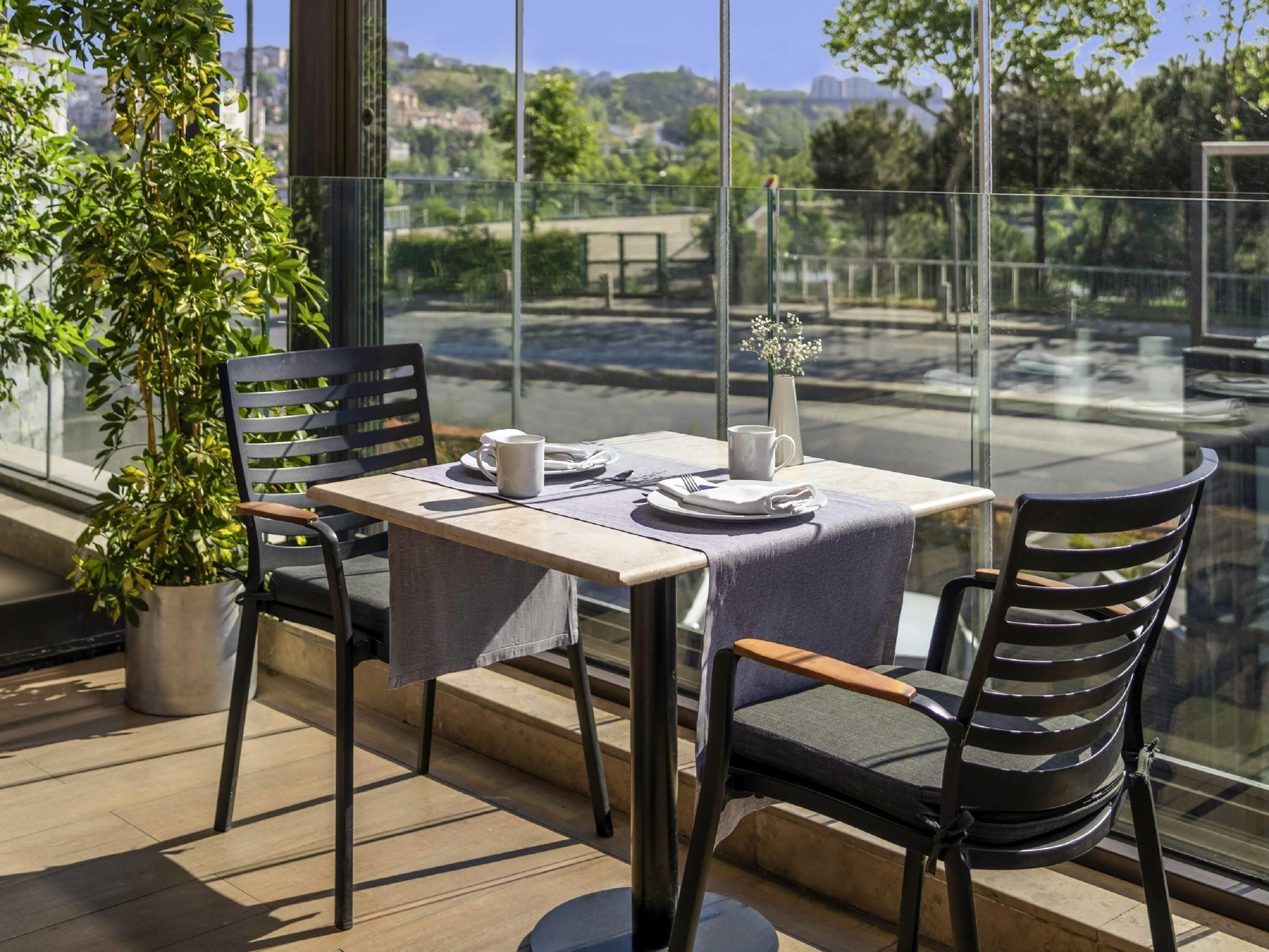Una mesa de comedor con sillas, una planta en maceta y vistas a un puente y follaje.