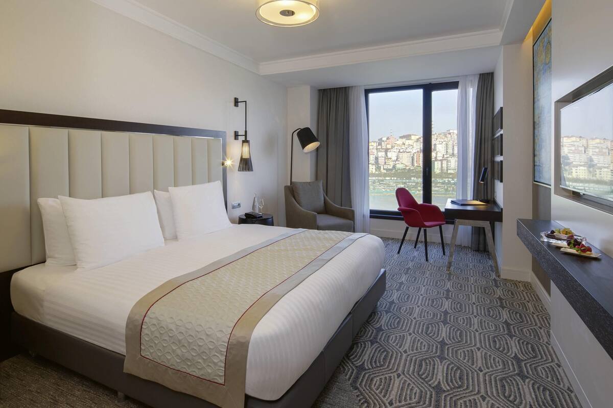 Una habitación de hotel con una cama grande, un escritorio, una silla y vistas a la ciudad.