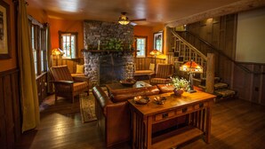 A cozy living room with a stone fireplace, wooden furniture, and a staircase.