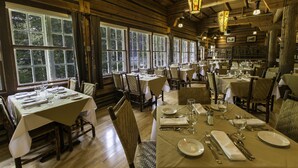 A restaurant with multiple tables set for dining, wooden walls, and large windows.