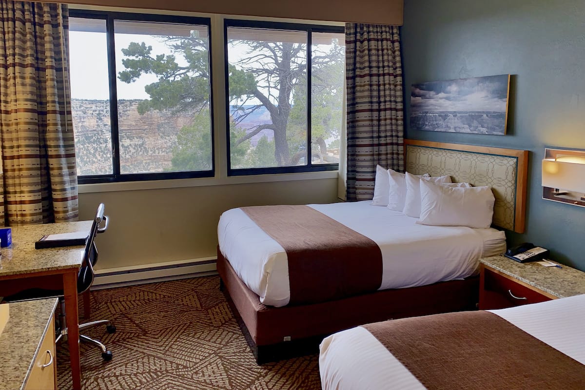 A hotel room with a large bed, a desk, and a view of a canyon through the window.