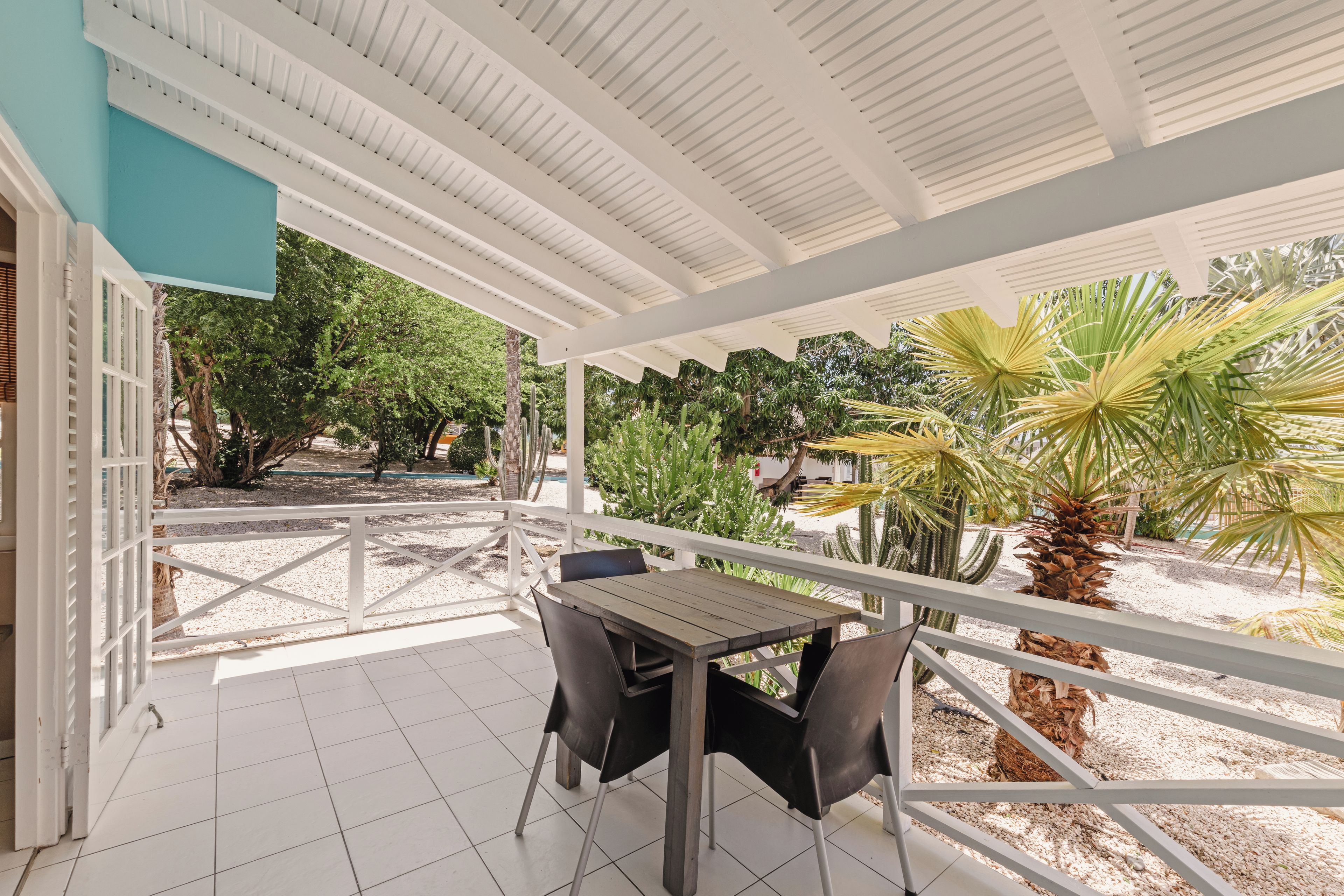 Eine überdachte Terrasse im Freien mit Tisch und Stühlen, umgeben von einem weißen Geländer und verschiedenen Pflanzen.