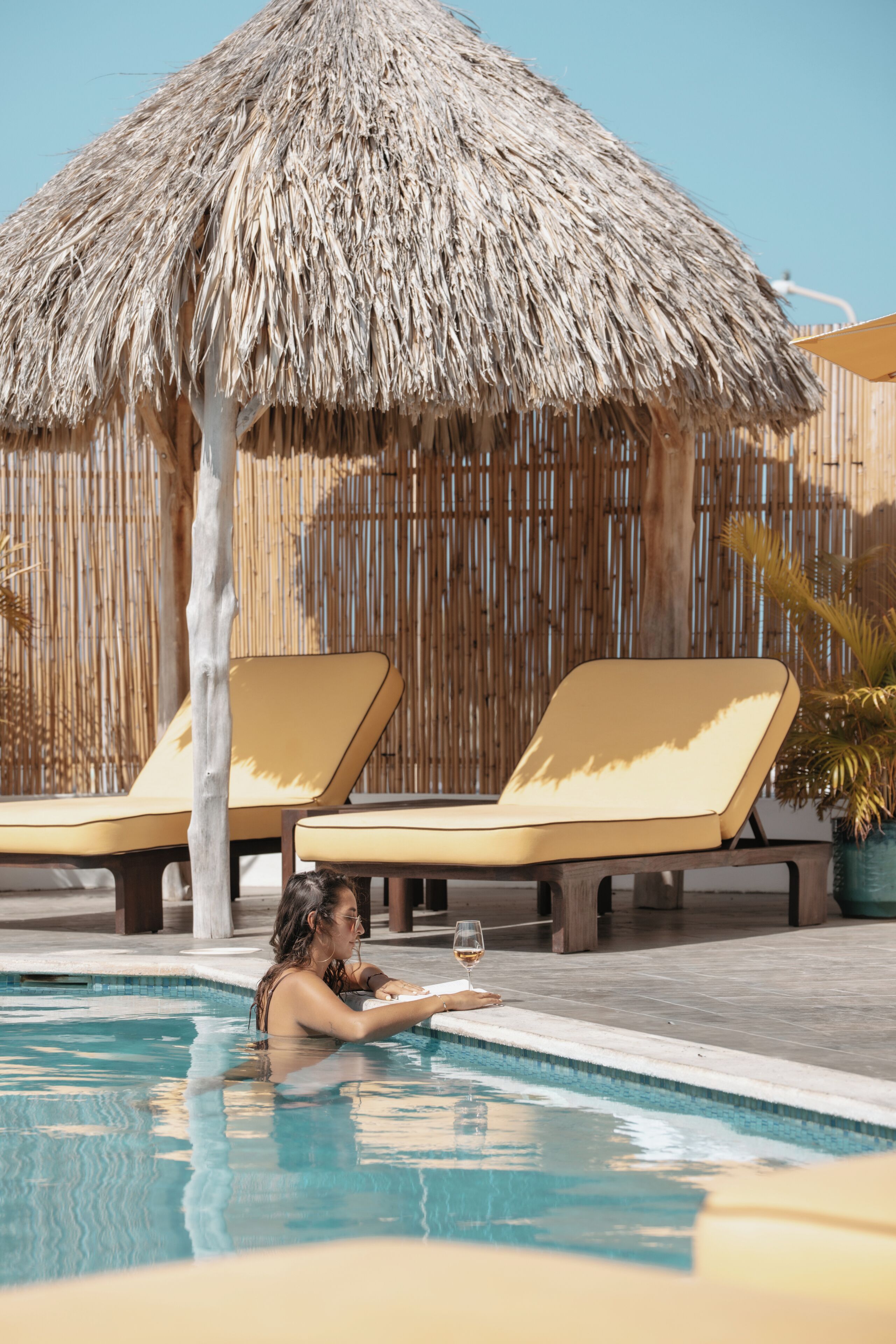 A pool area with lounge chairs, a thatched umbrella, and a potted plant.