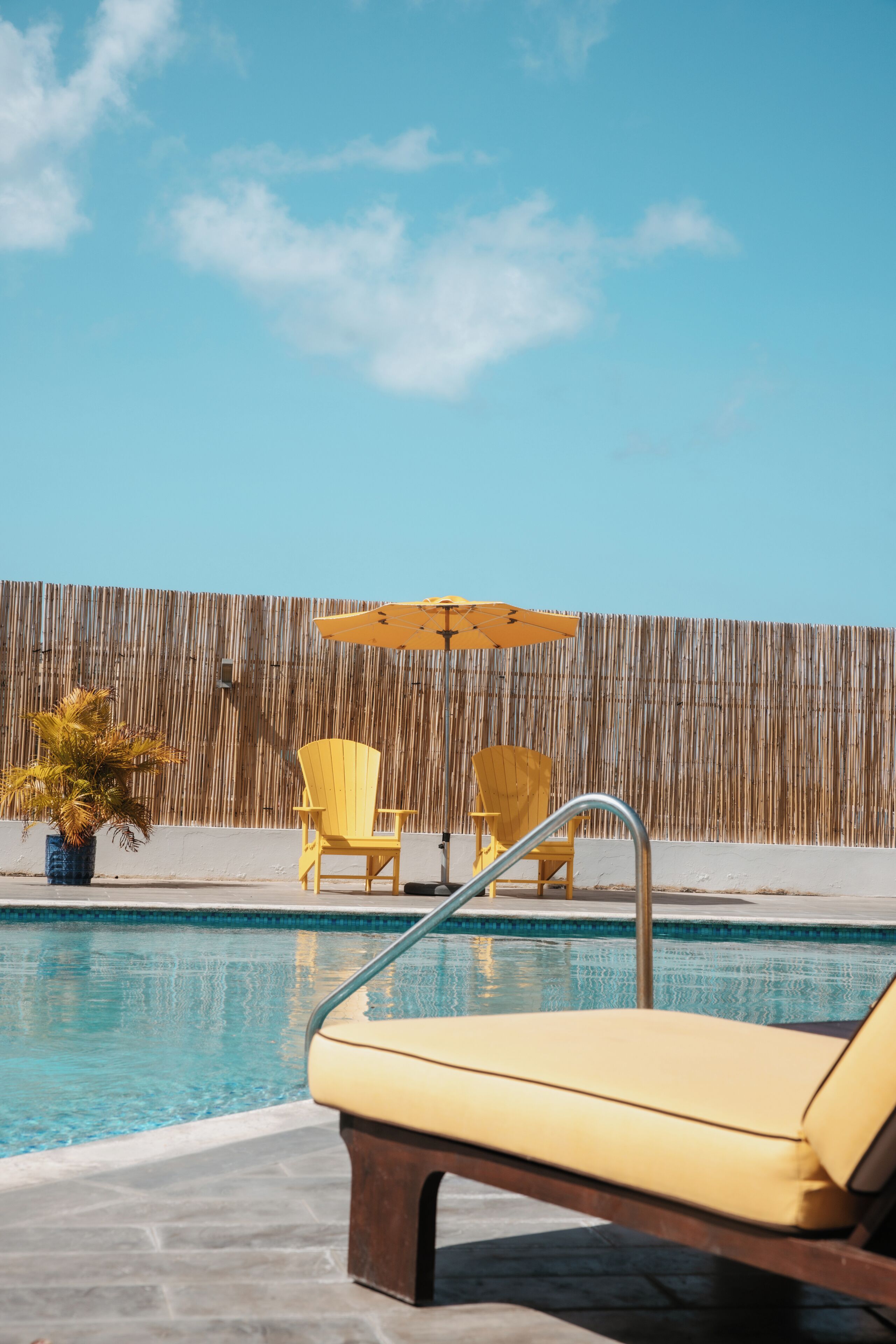 A poolside area with lounge chairs, a small umbrella, and a bamboo fence.