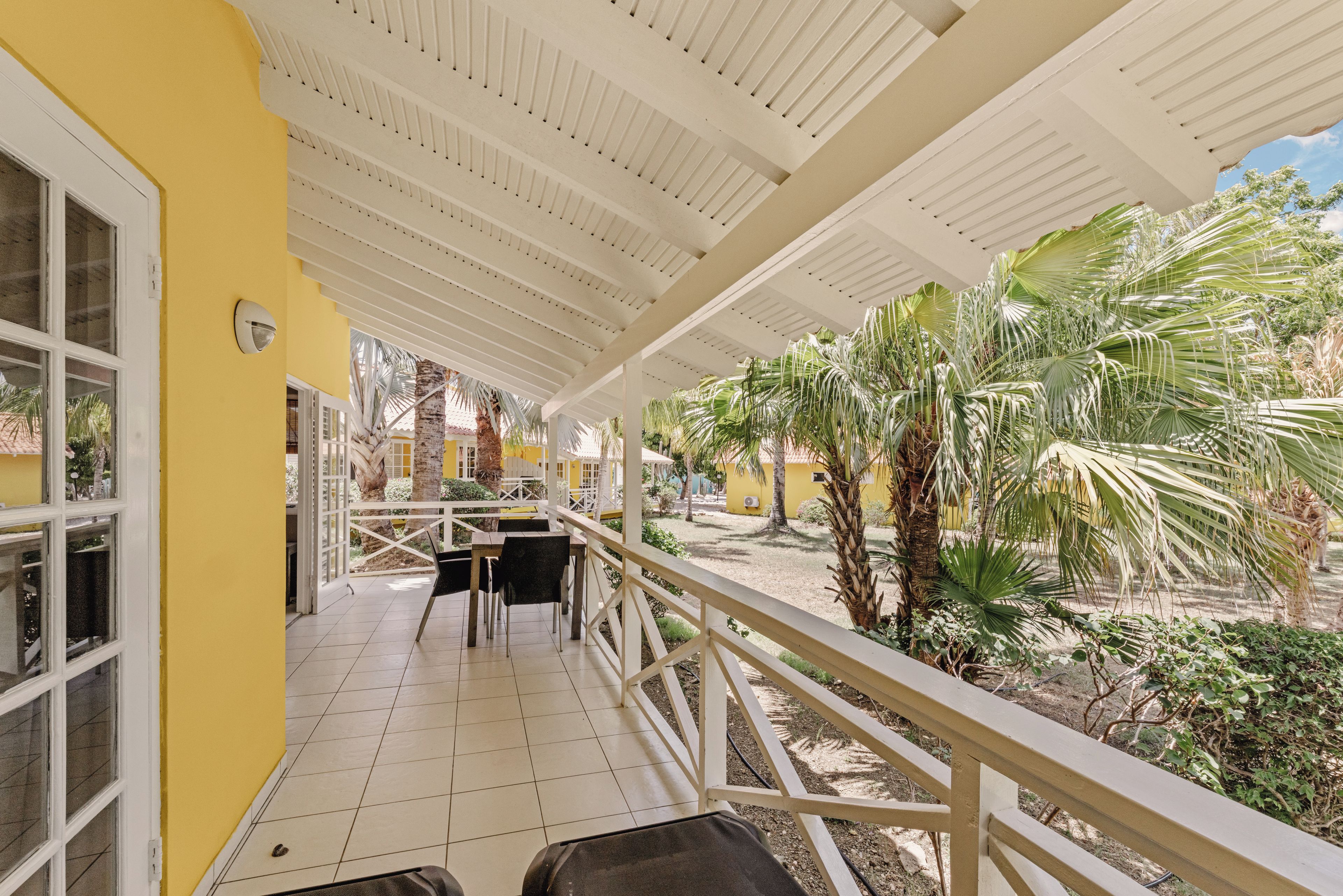 A covered outdoor area with a tiled floor, a railing, and a view of a yellow building.