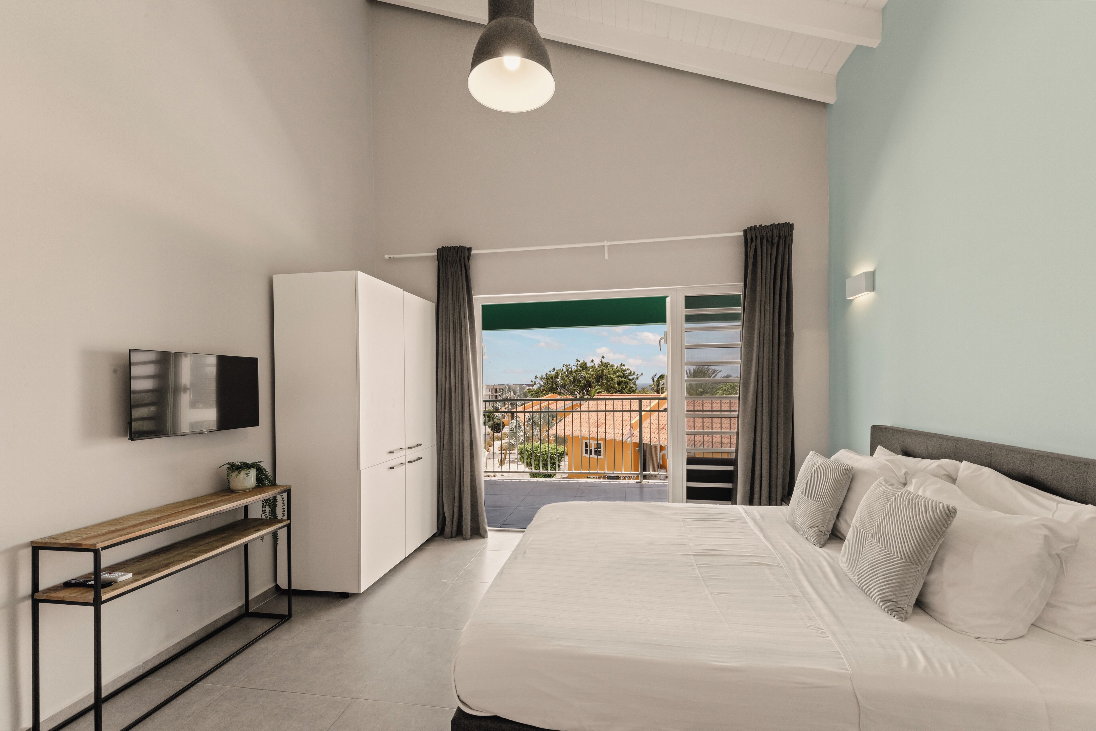 A modern bedroom with a bed, a TV, a console table, and a view of the outside.