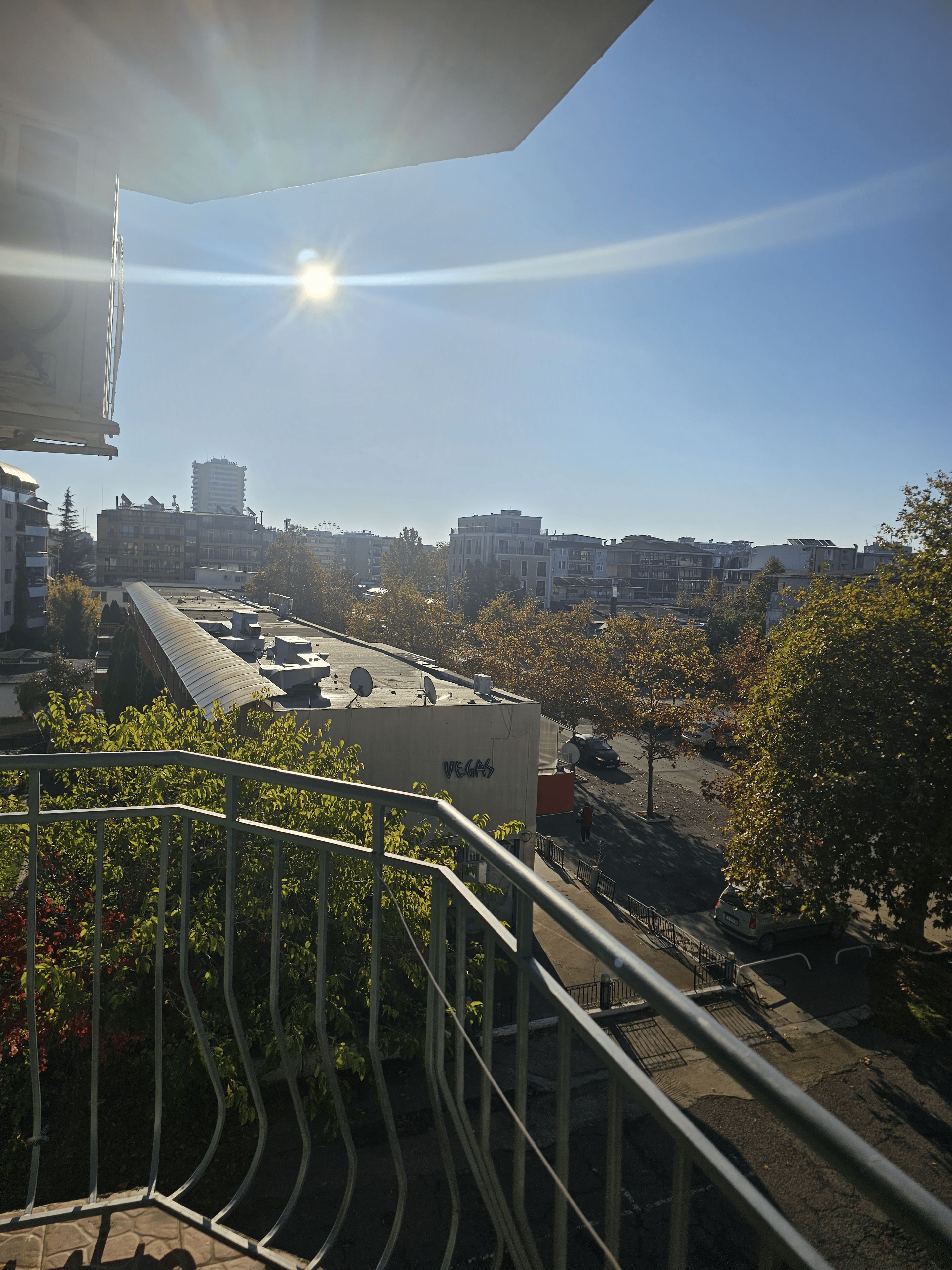Un paisaje urbano con cielo despejado, edificios y una calle con coches estacionados.