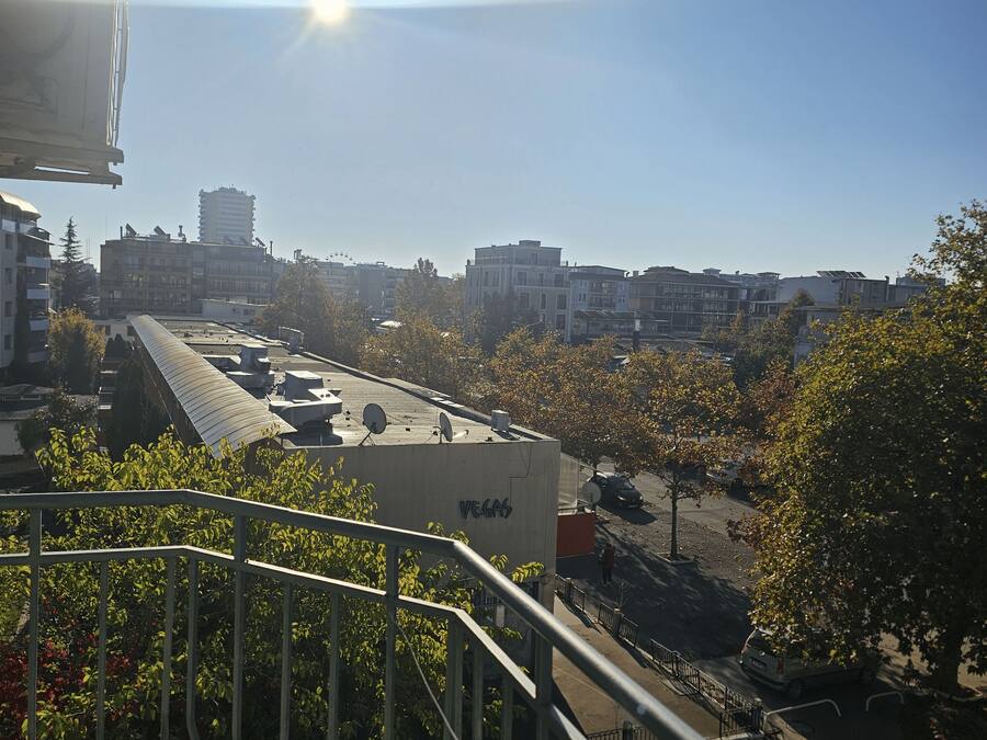 A cityscape with a clear sky, buildings, and a street with parked cars.