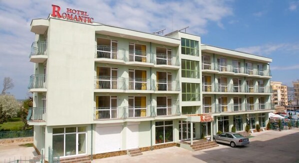 Un hôtel à plusieurs étages doté de balcons, d’un parking et offrant une vue sur un ciel dégagé.