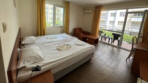A hotel room with a double bed, a desk, a chair, and a balcony with a view of buildings. - Family Hotel Romantic (Sunny Beach)