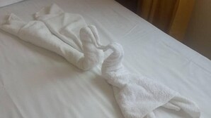 A neatly made bed with a towel arranged in a swan shape. - Family Hotel Romantic (Sunny Beach)