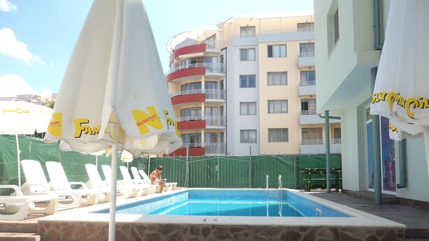 A swimming pool area with lounge chairs and umbrellas, surrounded by multi-story buildings. - Family Hotel Romantic (Sunny Beach)