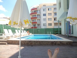 A swimming pool area with lounge chairs and umbrellas, surrounded by multi-story buildings. - Family Hotel Romantic (Sunny Beach)
