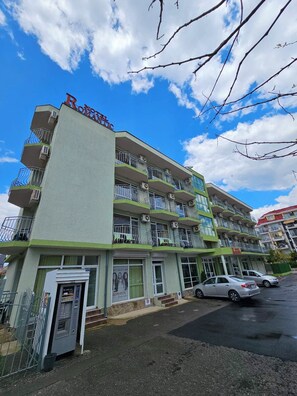 A multi-story hotel with balconies, a parking area, and a clear sky. - Family Hotel Romantic (Sunny Beach)