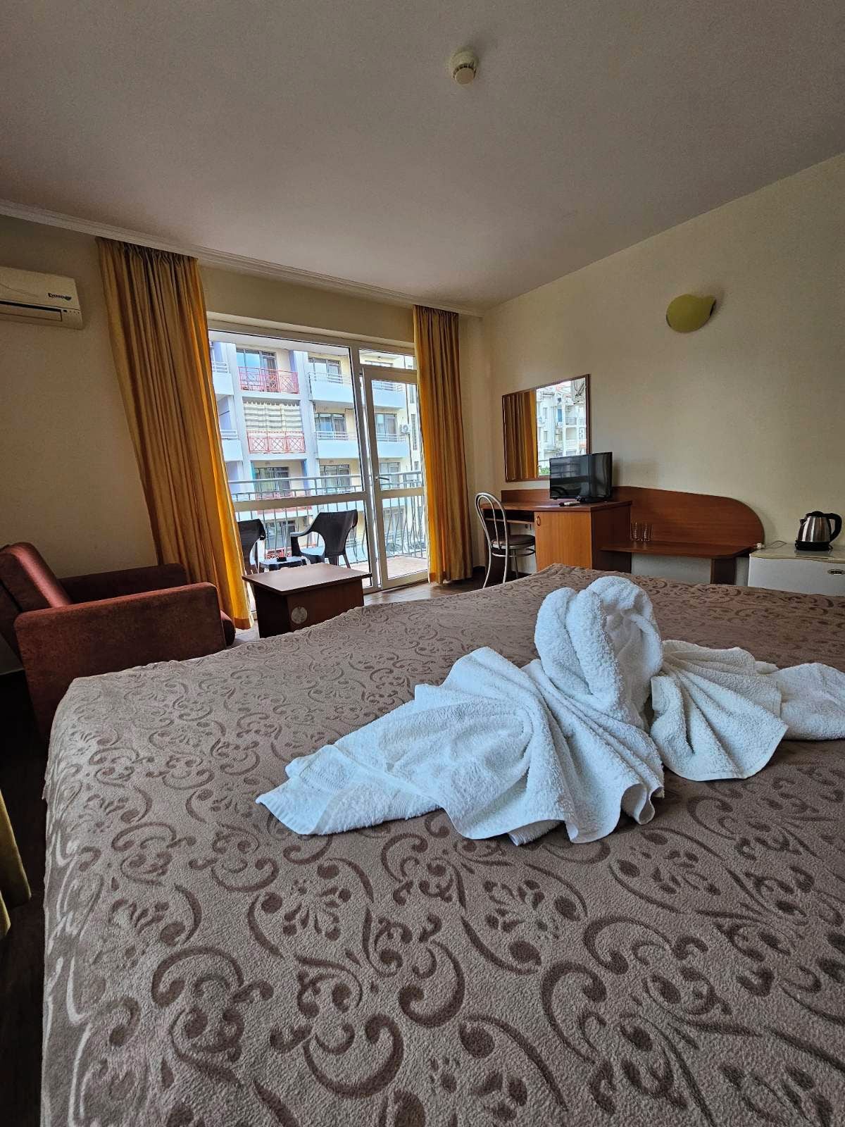 A hotel room with a bed, a desk, a chair, a television, and a view of the outside.