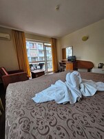 Habitación de hotel con cama, escritorio, silla, televisor y vista al exterior.
