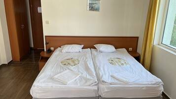 A double bed with two pillows and a small bedside table, a wooden wardrobe, and a framed picture on the wall.