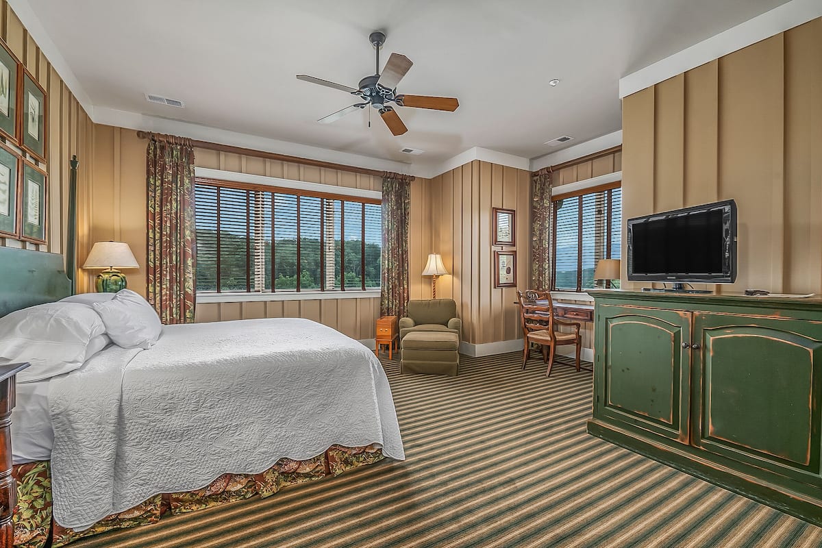 A hotel room with a bed, a desk, a television, and a ceiling fan.