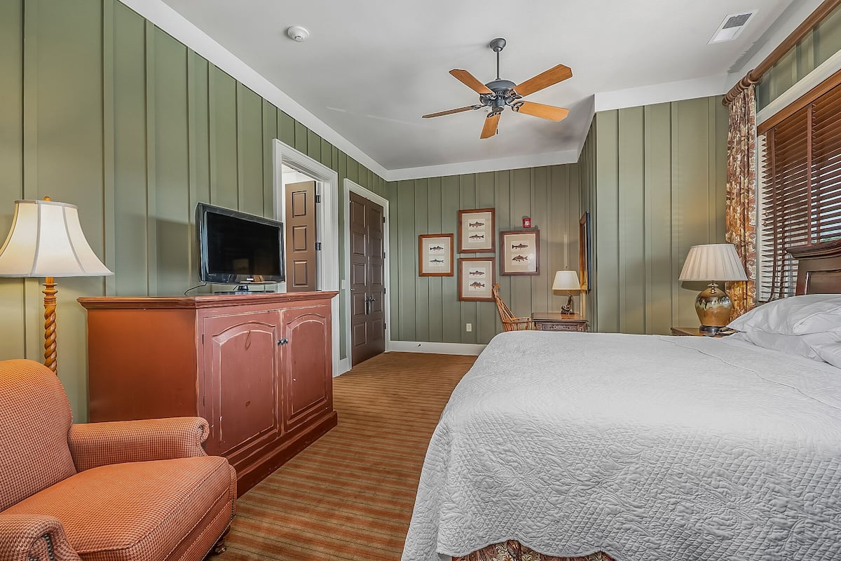 A hotel room with a bed, a television, a wooden cabinet, a chair, and a ceiling fan.