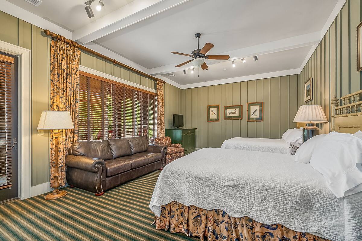 A hotel room with a large bed, a sofa, a ceiling fan, and a window with blinds.