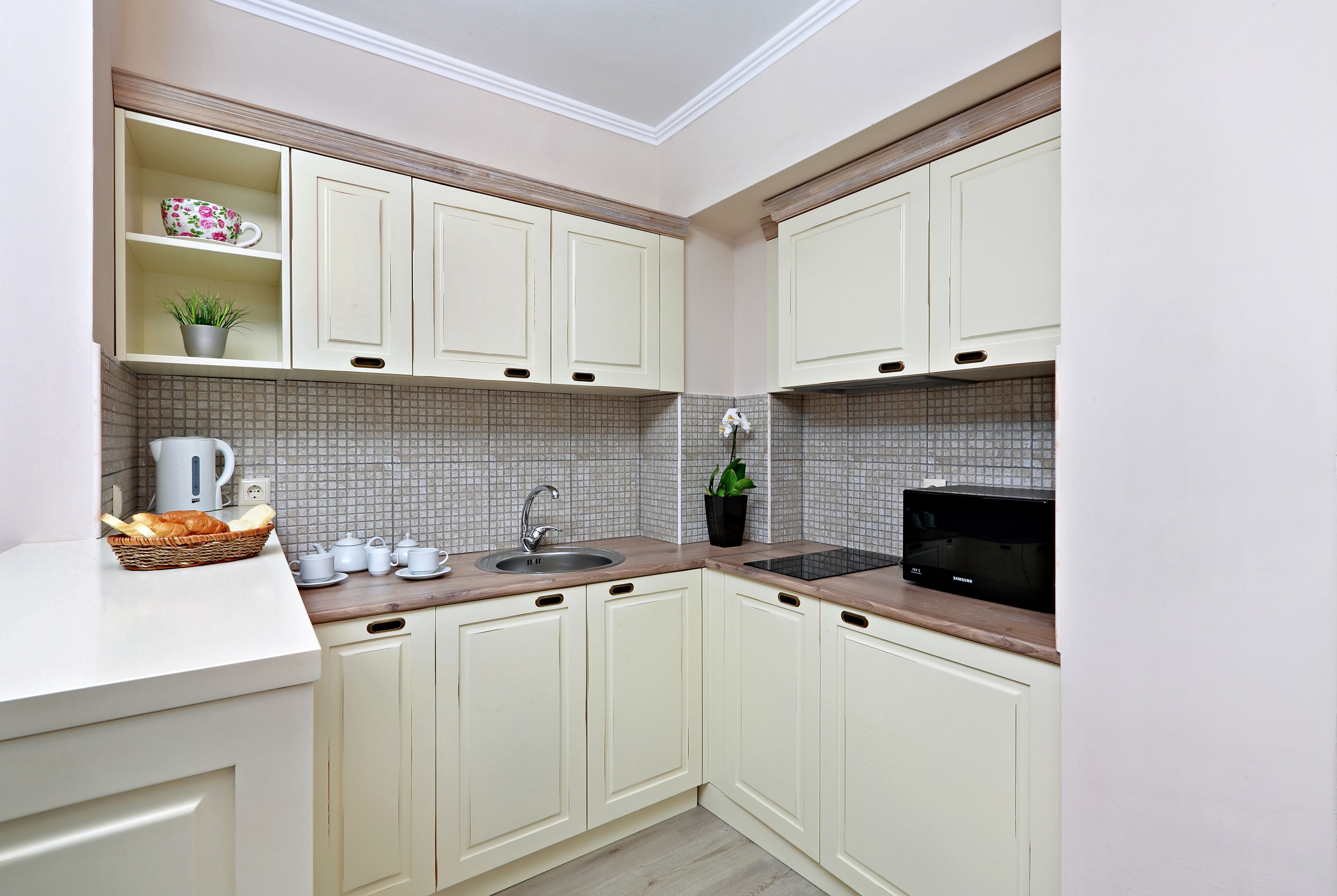 A compact kitchen with white cabinets, a tiled backsplash, a microwave, and a sink.