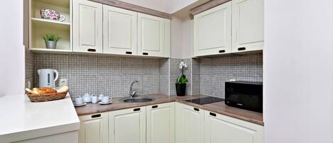 A compact kitchen with white cabinets, a tiled backsplash, a microwave, and a sink.