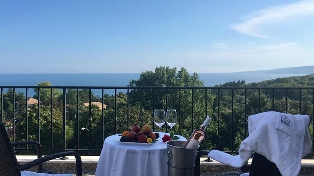 A balcony with a table set for two, featuring a fruit platter, wine glasses, and a bottle of wine. - White Rock Castle Suite Hotel & Wellness Club (Balchik)