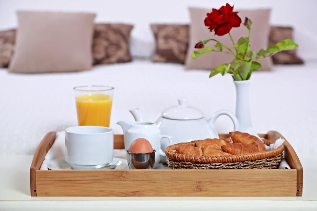 A breakfast tray with croissants, a glass of orange juice, a teapot, a cup, and a small egg on a wooden tray.