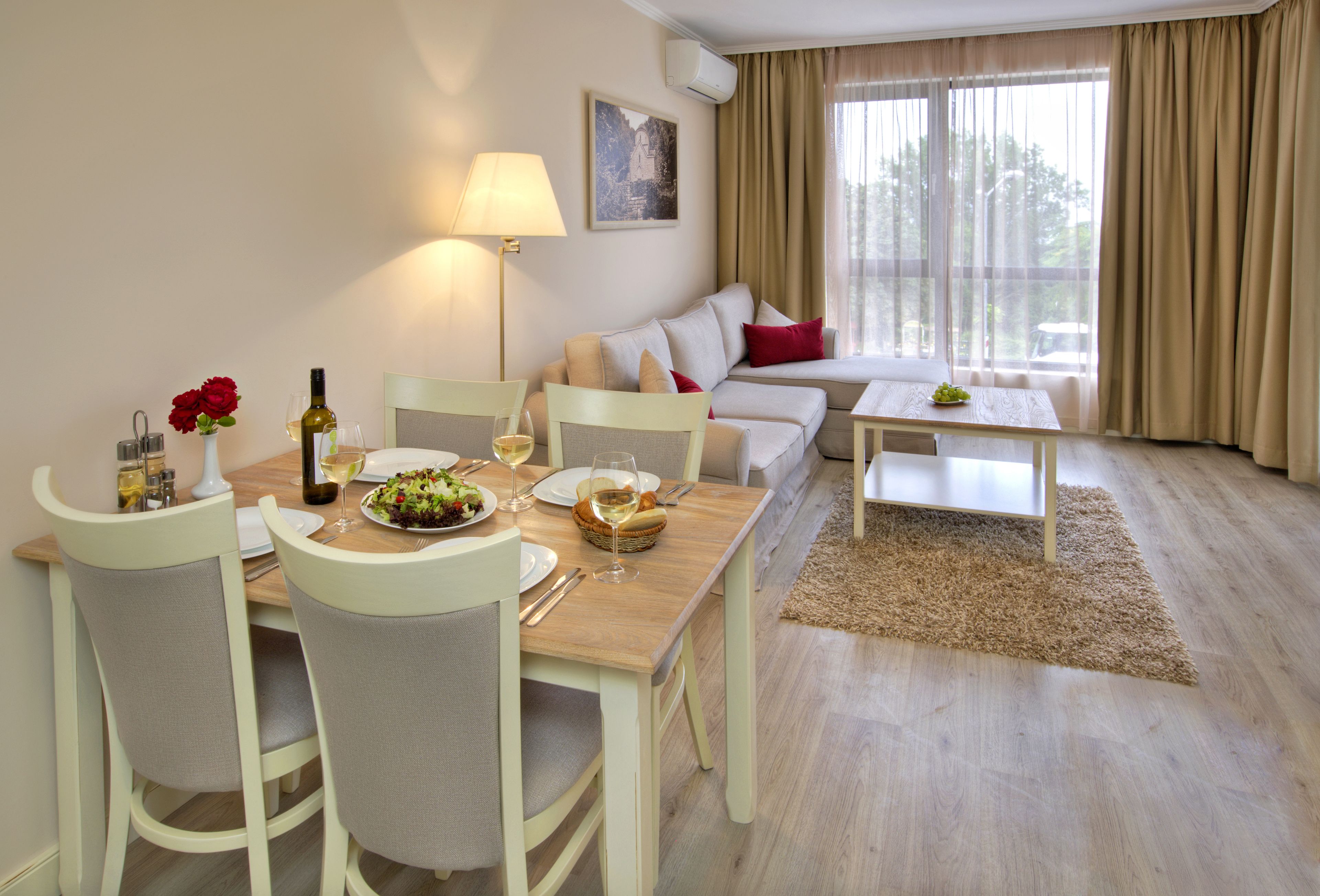 Comedor con una mesa lista para dos personas, un sofá y una ventana con cortinas.