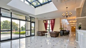 A spacious lobby with a high ceiling, large windows, and a modern chandelier. - White Rock Castle Suite Hotel & Wellness Club (Balchik)