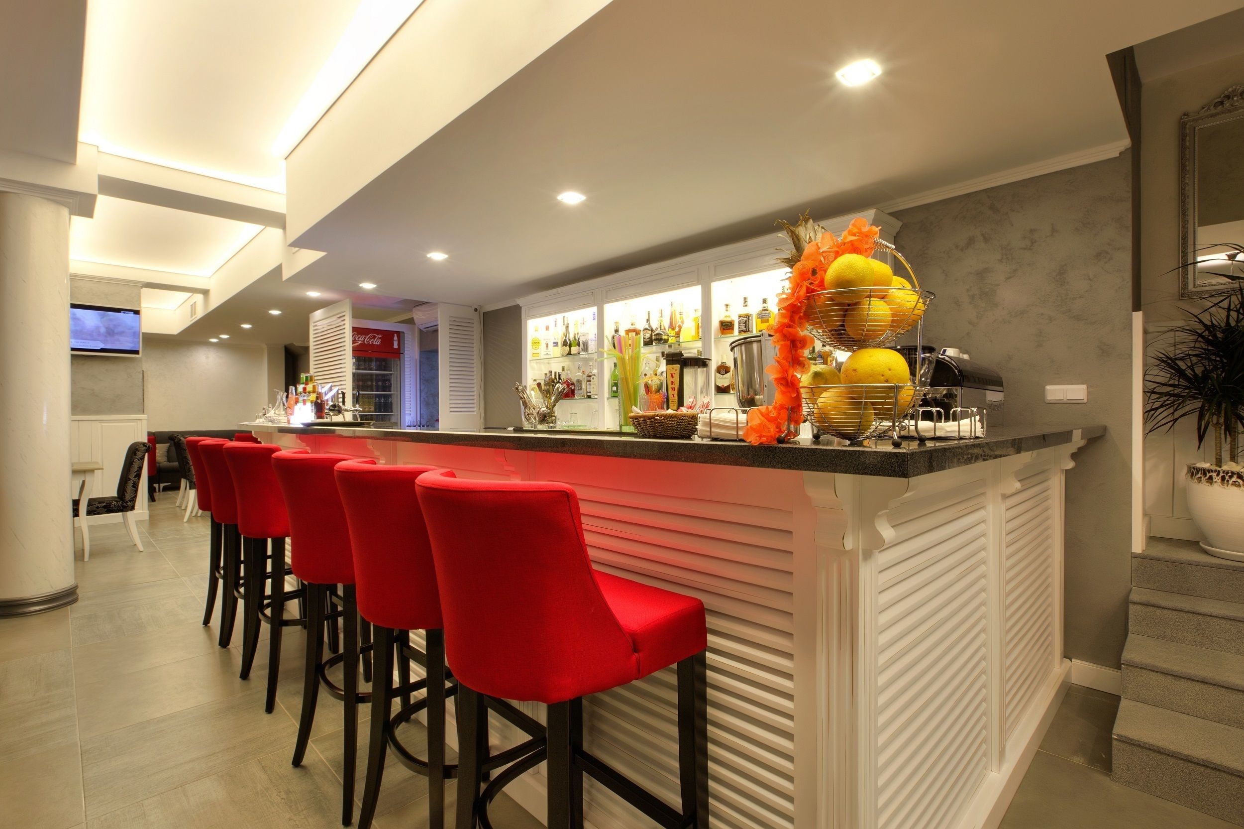 A modern bar area with a counter, red bar stools, and a variety of bottles and glasses.