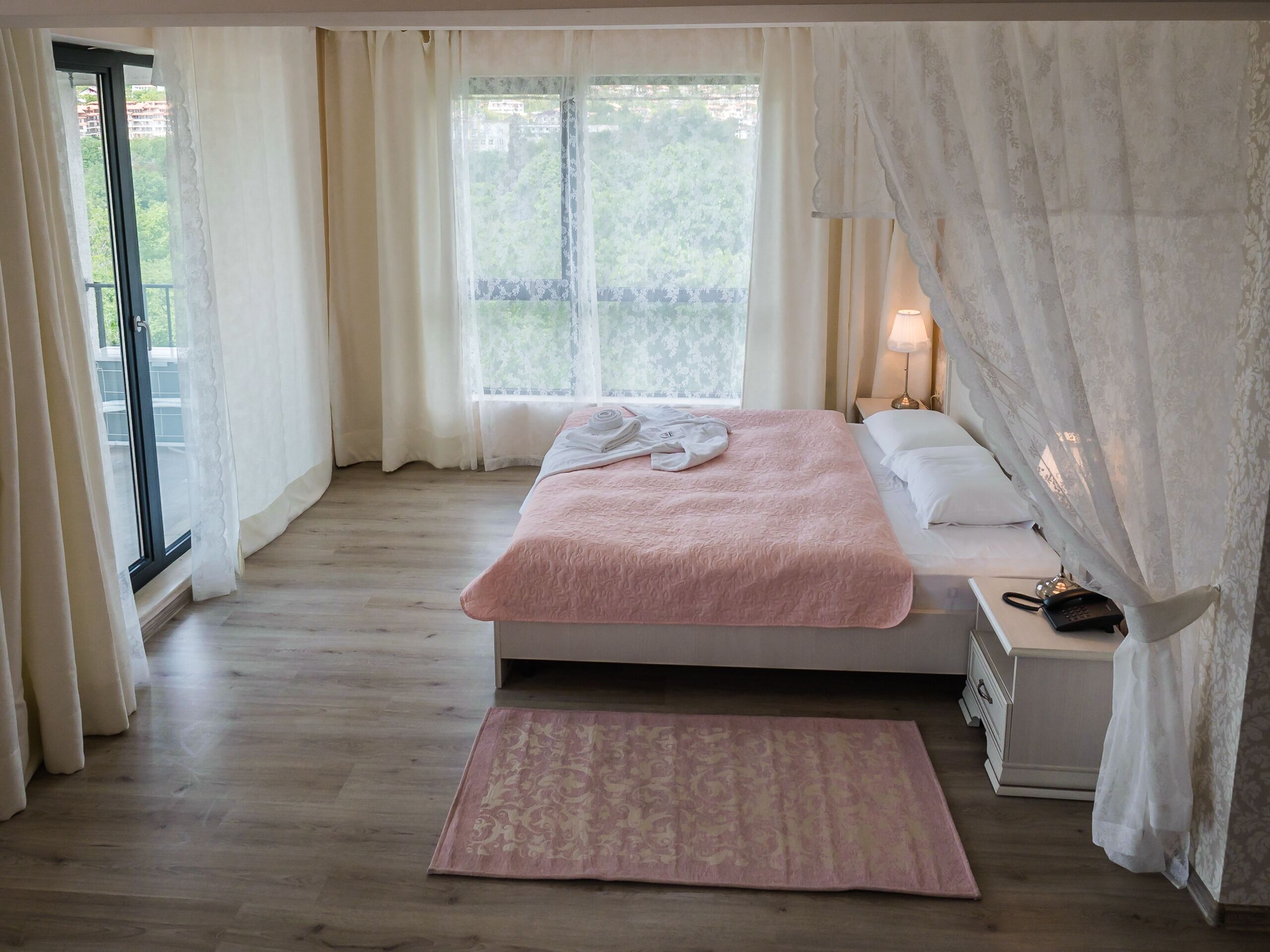 A bedroom with a bed, a nightstand, a lamp, a phone, and a window with curtains.