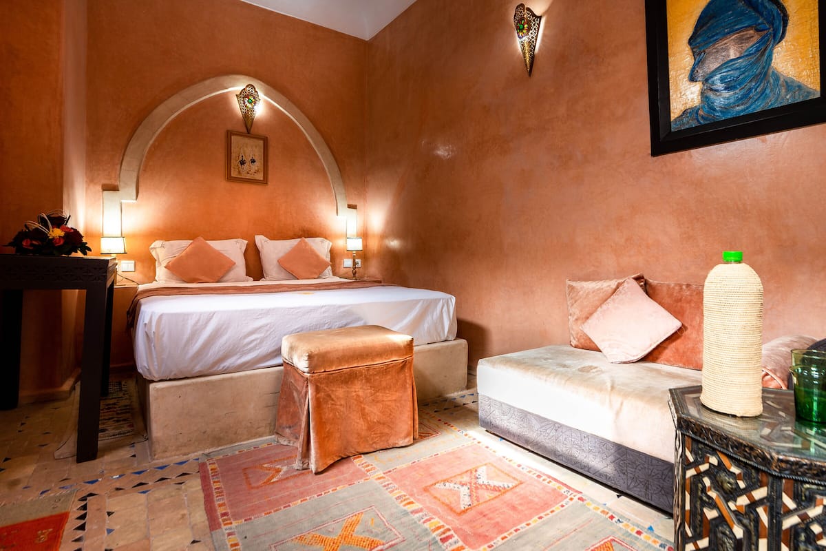 Une chambre d’hôtel avec un lit, une petite table, une chaise, un élément décoratif mural et un tapis à motifs.