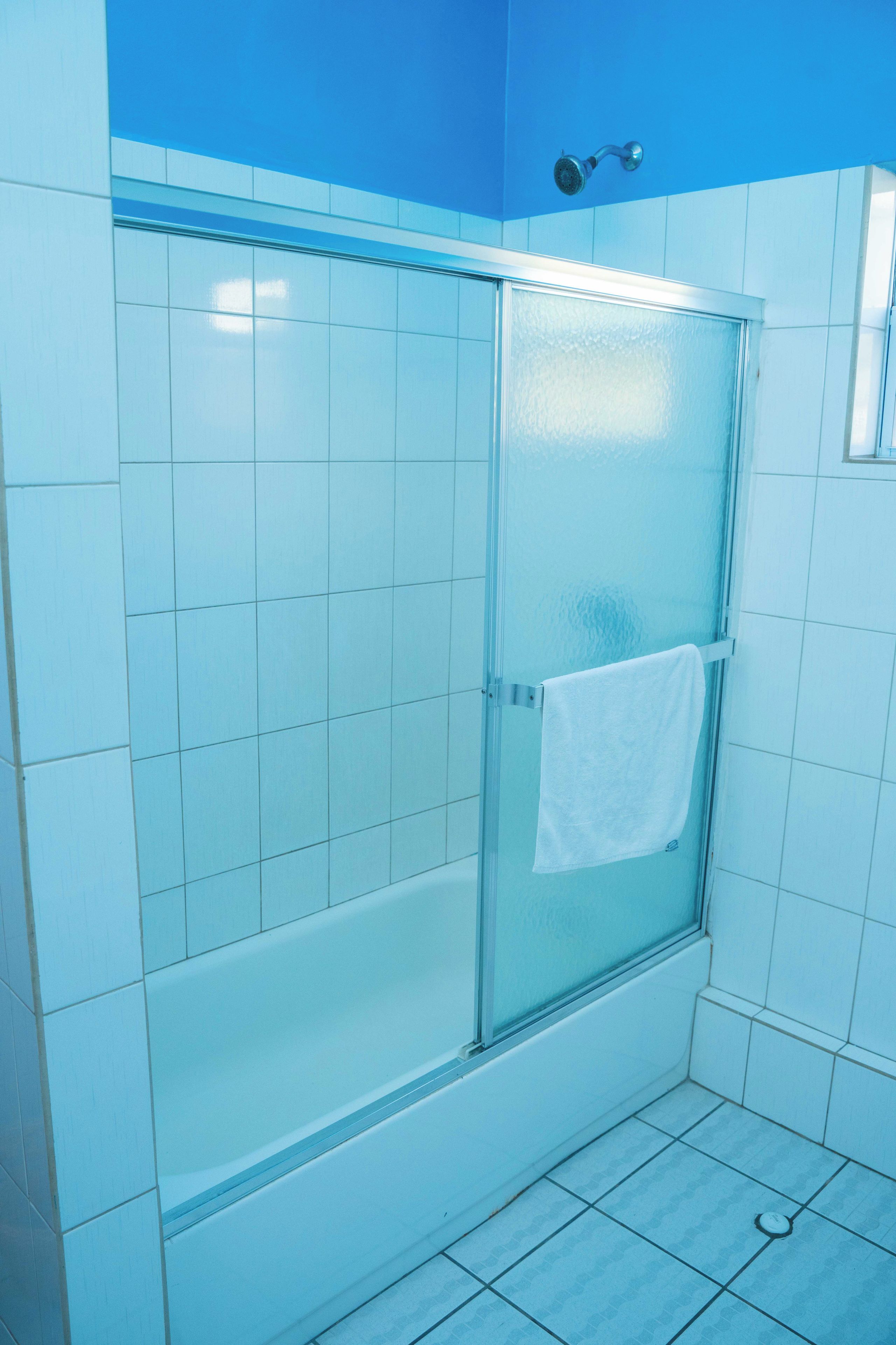 A bathroom with a glass shower enclosure, white tiles, and a towel hanging on the door.