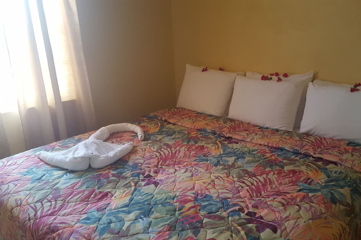 Una cama con una colcha de estampado floral, almohadas blancas y una toalla blanca con forma de cisne.
